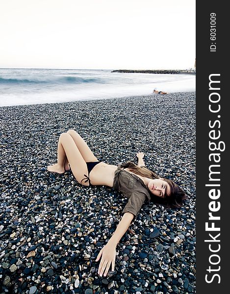 Beautiful woman laying on the beach with sad gesture. Long exposed waves.