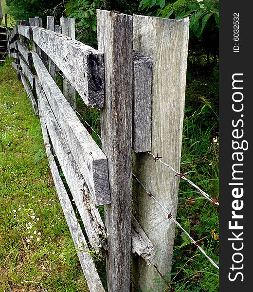 A weathered gray-wood farm fence strung with barbed wire. A weathered gray-wood farm fence strung with barbed wire