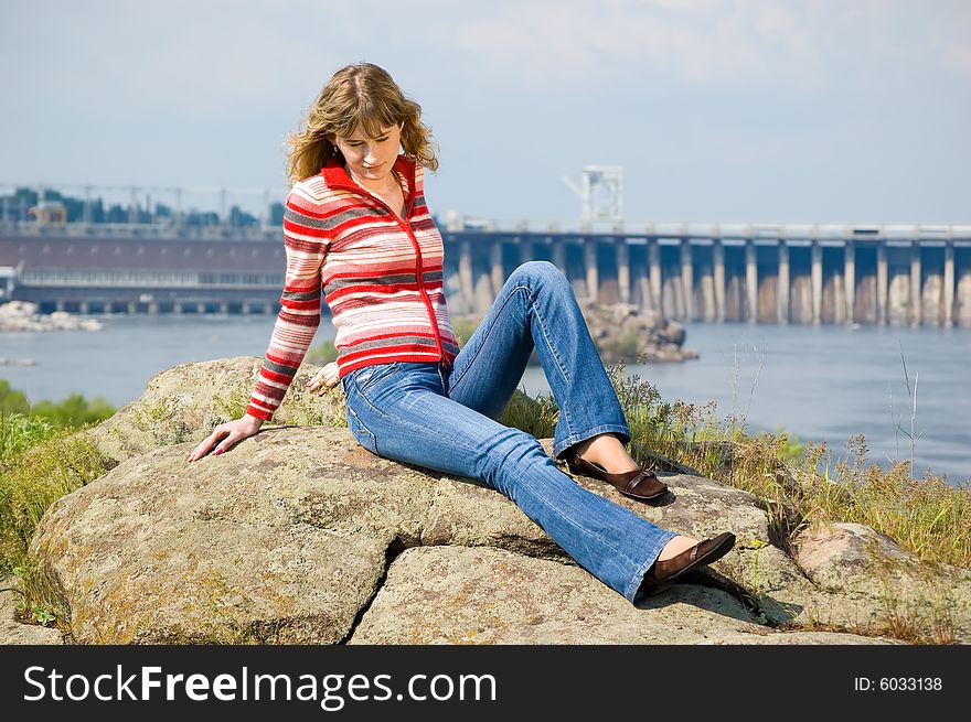 The girl sits on stones against hydroelectric power station. Zaporozhye. Ukraine. The girl sits on stones against hydroelectric power station. Zaporozhye. Ukraine