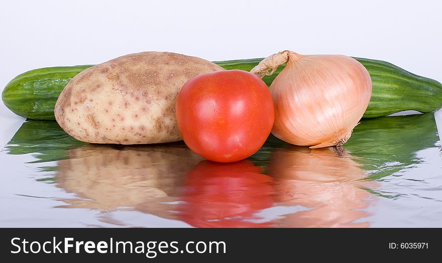 A potato, tomato, onion, and a cucumber reflected on aluminum foil. A potato, tomato, onion, and a cucumber reflected on aluminum foil