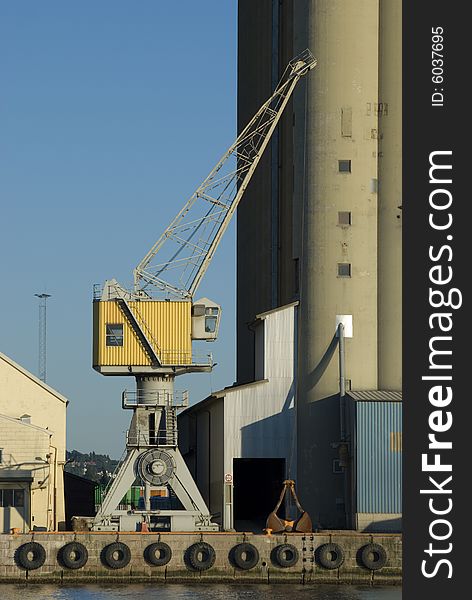 Crane at a harbour, between a warehouse and a silo. Crane at a harbour, between a warehouse and a silo.