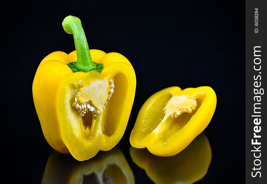 A yellow bell pepper that's been sliced open to reveal the insides including the seeds.  It sits isolated on a solid black background with a soft reflection below it. A yellow bell pepper that's been sliced open to reveal the insides including the seeds.  It sits isolated on a solid black background with a soft reflection below it.