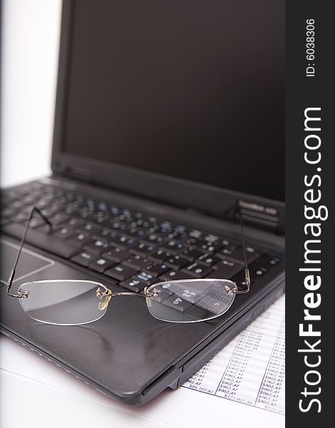 Black laptop, glasses, pen, sheet on the white background
