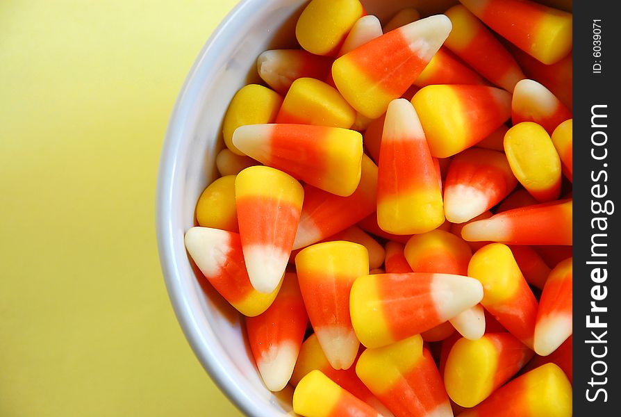 White bowl of candy corn on yellow background