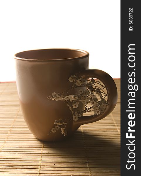 A brown coffee mug isolated on a bamboo table place mat with dried flowers. A brown coffee mug isolated on a bamboo table place mat with dried flowers