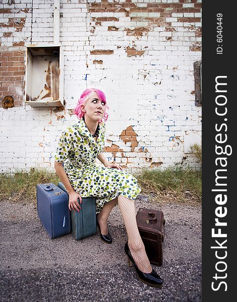 Woman with pink hair wearing polka dot dress in alley with suitcases. Woman with pink hair wearing polka dot dress in alley with suitcases