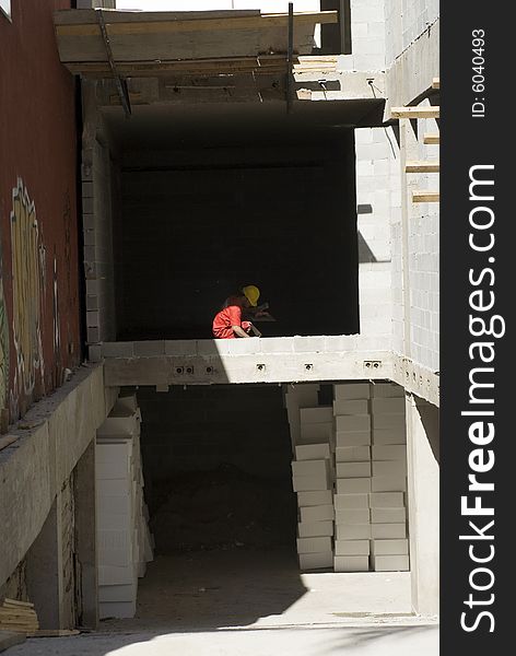 Construction worker squats on second floor of construction site. He is far away in the shadow. Vertically framed photo. Construction worker squats on second floor of construction site. He is far away in the shadow. Vertically framed photo.
