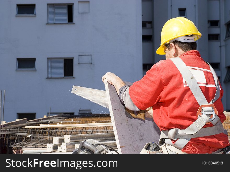 Construction worker holds board while cutting with a hand saw. Horizontally framed photo. Construction worker holds board while cutting with a hand saw. Horizontally framed photo.