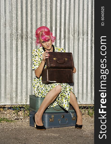 Woman with pink hair wearing polka dot dress in alley with suitcases. Woman with pink hair wearing polka dot dress in alley with suitcases