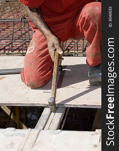 Construction worker pulling board with hammer. He is kneeling on the board. Vertically framed photo. Construction worker pulling board with hammer. He is kneeling on the board. Vertically framed photo.