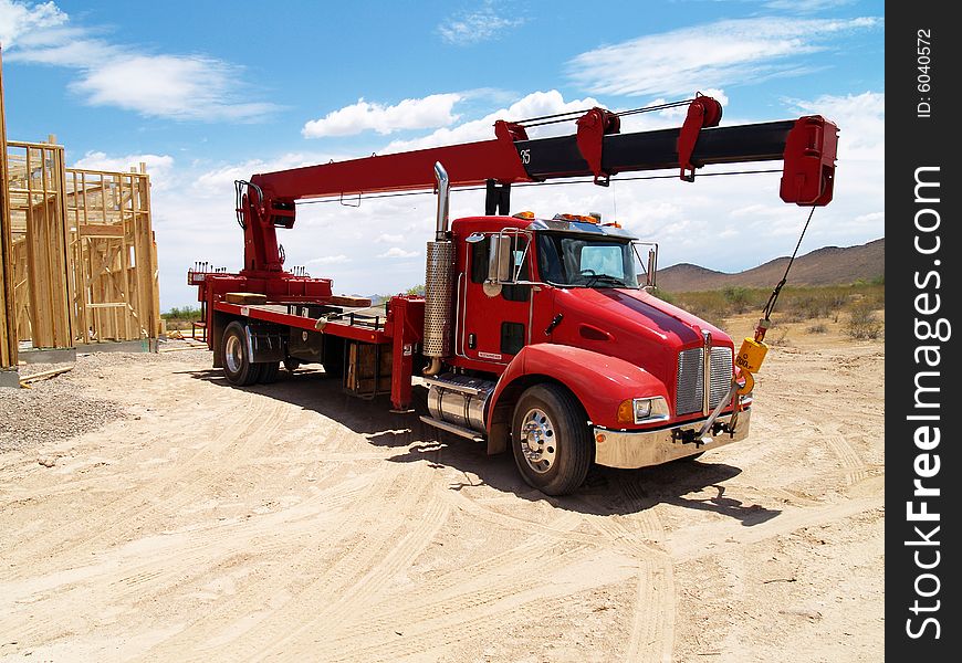 Red semi truck with a crane on it in a construction site with a house frame in the background. Horizontally framed photo. Red semi truck with a crane on it in a construction site with a house frame in the background. Horizontally framed photo.