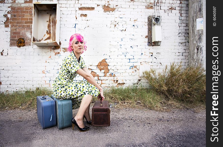 Woman with pink hair wearing polka dot dress in alley with suitcases. Woman with pink hair wearing polka dot dress in alley with suitcases