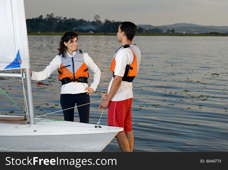 A couple is standing in the lake water next to their sailboat.  They are smiling and looking at each other.  Horizontally framed shot. A couple is standing in the lake water next to their sailboat.  They are smiling and looking at each other.  Horizontally framed shot.