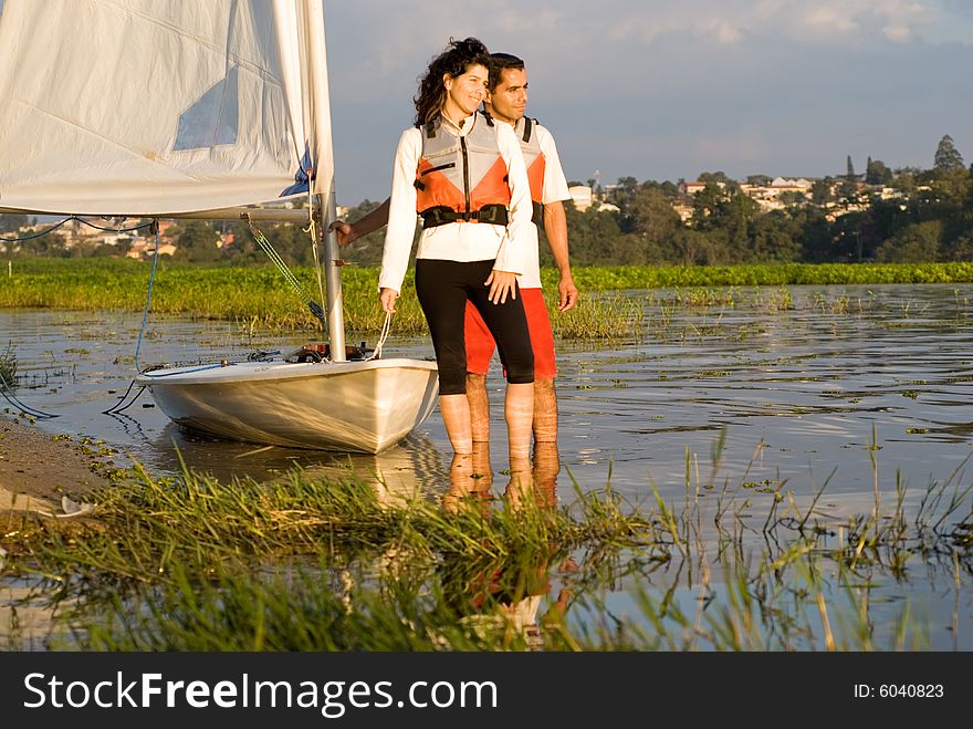 A woman and man are next to a sailboat.  They are smiling and looking away from the camera.  Horizontally framed shot. A woman and man are next to a sailboat.  They are smiling and looking away from the camera.  Horizontally framed shot.