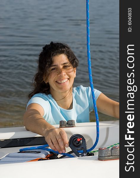 A young woman is leaning over and fixing something on her sailboat.  She is smiling and looking at the camera.  Vertically framed shot. A young woman is leaning over and fixing something on her sailboat.  She is smiling and looking at the camera.  Vertically framed shot.