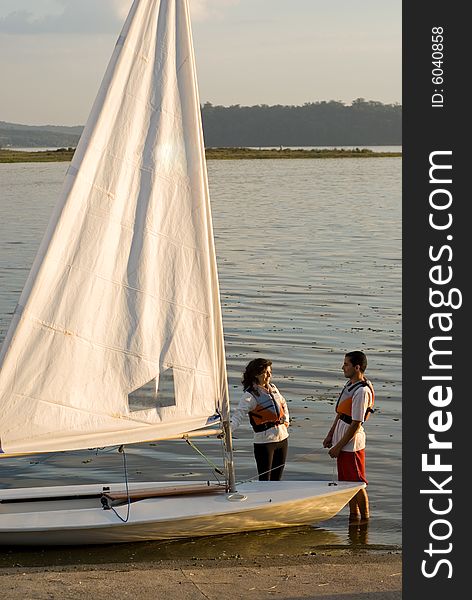 A couple is standing in the lake water next to their sailboat.  They are looking at each other.  Vertically framed shot. A couple is standing in the lake water next to their sailboat.  They are looking at each other.  Vertically framed shot.