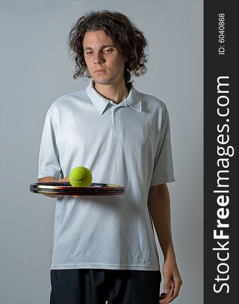 Male athlete holding a tennis racket and balancing a ball on it.  He is looking at the tennis ball.  Vertically framed shot. Male athlete holding a tennis racket and balancing a ball on it.  He is looking at the tennis ball.  Vertically framed shot.