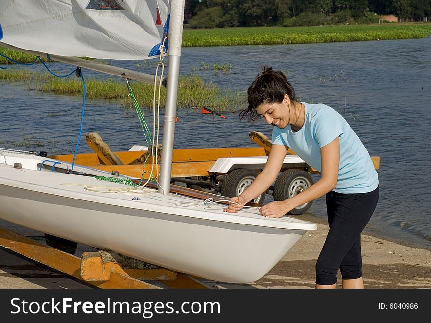 A woman is fixing the sail on their sailboat.  She is smiling and looking at the ropes she is pulling.  Horizontally framed shot. A woman is fixing the sail on their sailboat.  She is smiling and looking at the ropes she is pulling.  Horizontally framed shot.