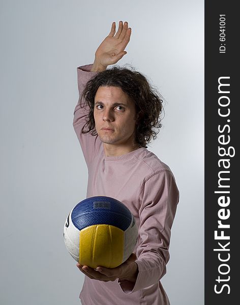 A man is in a studio posing with a volleyball.  He is about to spike the ball and is looking at the camera.  Vertically framed shot. A man is in a studio posing with a volleyball.  He is about to spike the ball and is looking at the camera.  Vertically framed shot.