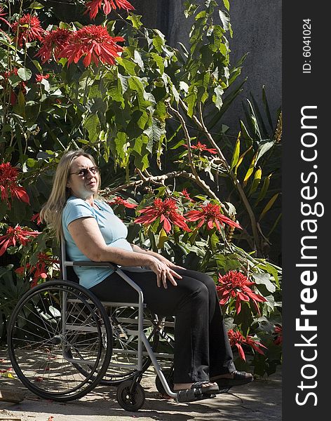 Woman sits outdoors in a wheelchair alongside flowers. Horizontally framed photo. Woman sits outdoors in a wheelchair alongside flowers. Horizontally framed photo.