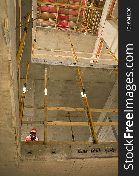 Construction worker smiles at camera from unfinished floor of a building under construction. Vertically framed photo. Construction worker smiles at camera from unfinished floor of a building under construction. Vertically framed photo.