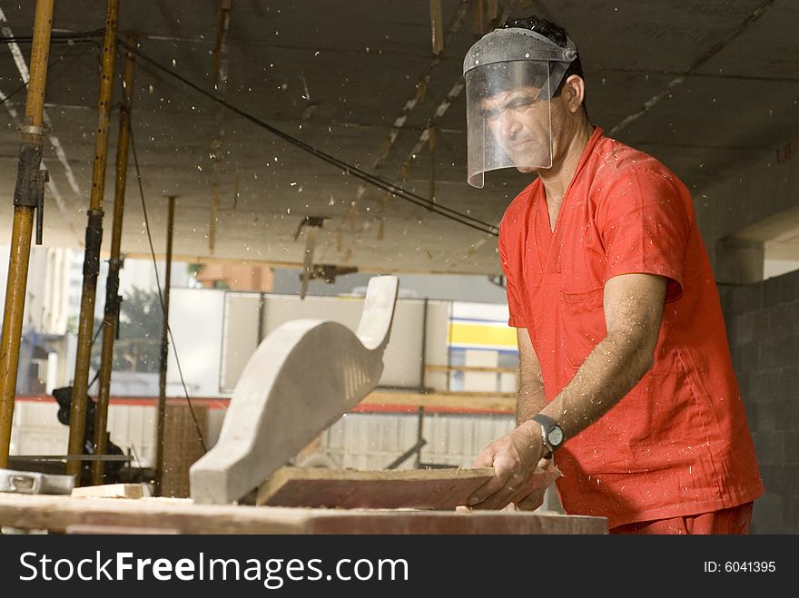 Construction worker cuts board on table saw while wearing face mask and orange suit. Horizontally framed photo. Construction worker cuts board on table saw while wearing face mask and orange suit. Horizontally framed photo.