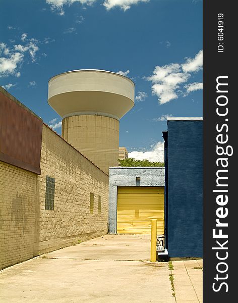 An alley with a view of a large water tower and colorful garage door. An alley with a view of a large water tower and colorful garage door.