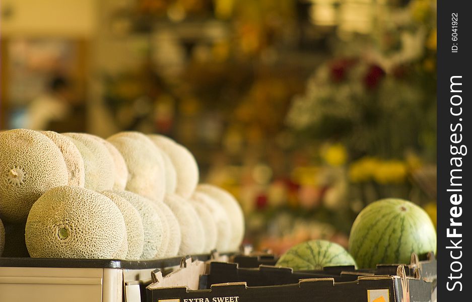 A stack of cantelopes and round watermelons in a grocery with flowers in the background. A stack of cantelopes and round watermelons in a grocery with flowers in the background.