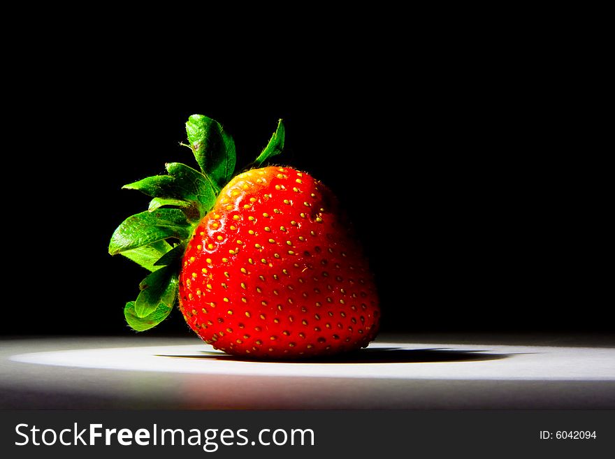 Lucious, ripe, red , juicy strawberry highlighted by a single spotlight against a dark background.