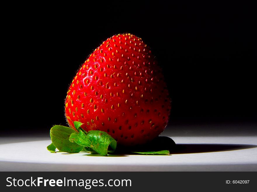 Lucious, ripe, red , juicy strawberry highlighted by a single spotlight against a dark background.