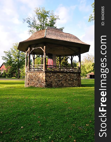 A rustic stone and wood bandstand in a small town park decorated with an American flag. A rustic stone and wood bandstand in a small town park decorated with an American flag.