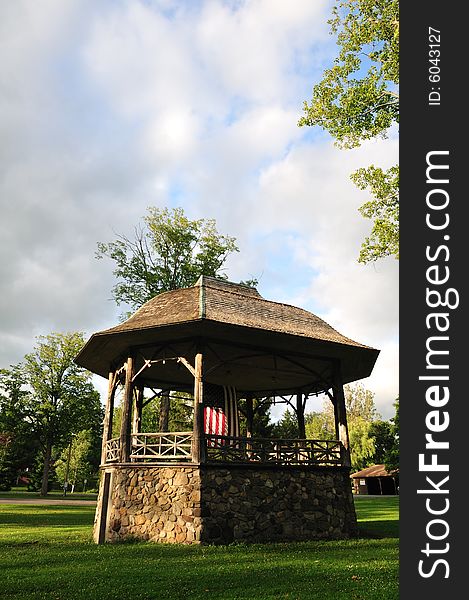 A rustic stone and wood bandstand in a small town park decorated with an American flag. A rustic stone and wood bandstand in a small town park decorated with an American flag.