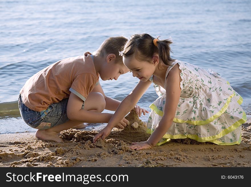 Cute small boy and girl playing in sand on seashore
