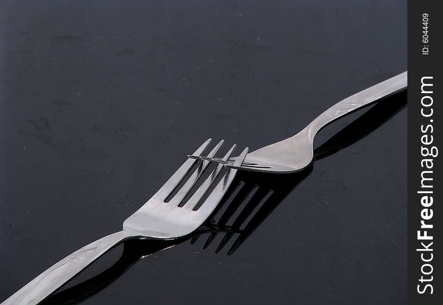 Two silver forks on a black shiny surface. Two silver forks on a black shiny surface