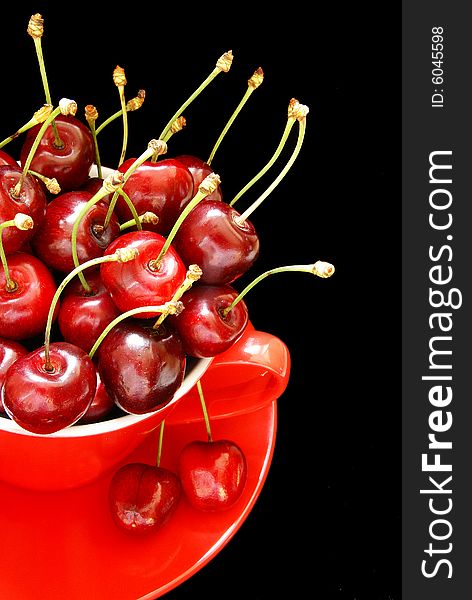 Red cherries in the red cup on the black background. Red cherries in the red cup on the black background