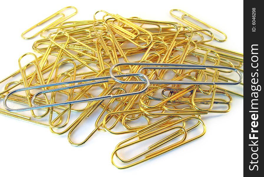 Heap of small gold writing paper clips. From above on it two big silver clips connected together lay on a white background. Heap of small gold writing paper clips. From above on it two big silver clips connected together lay on a white background.