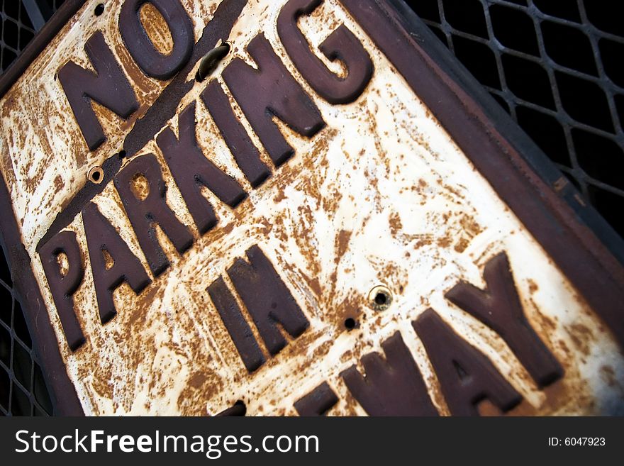 Street sign saying 'No Parking in Driveway' mounted on a metal grate of a gate.