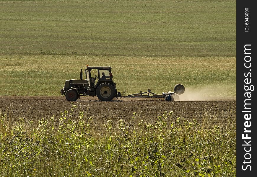 Green tractor drilling a field at summer time producing a lot of dust. Green tractor drilling a field at summer time producing a lot of dust