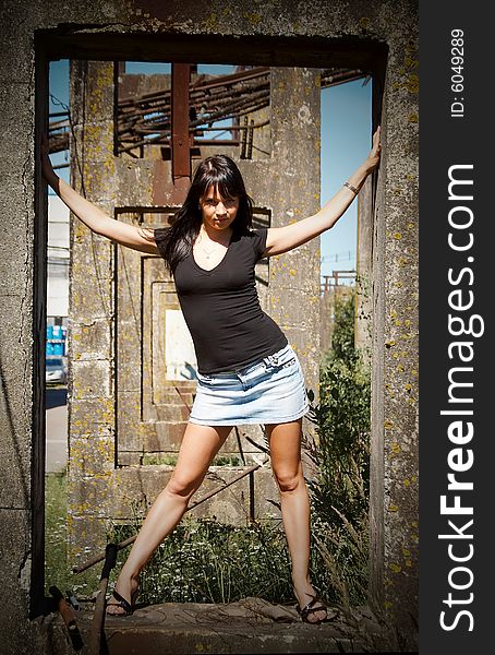 Young woman in jeans skirt standing on concrete structure of old factory. Young woman in jeans skirt standing on concrete structure of old factory