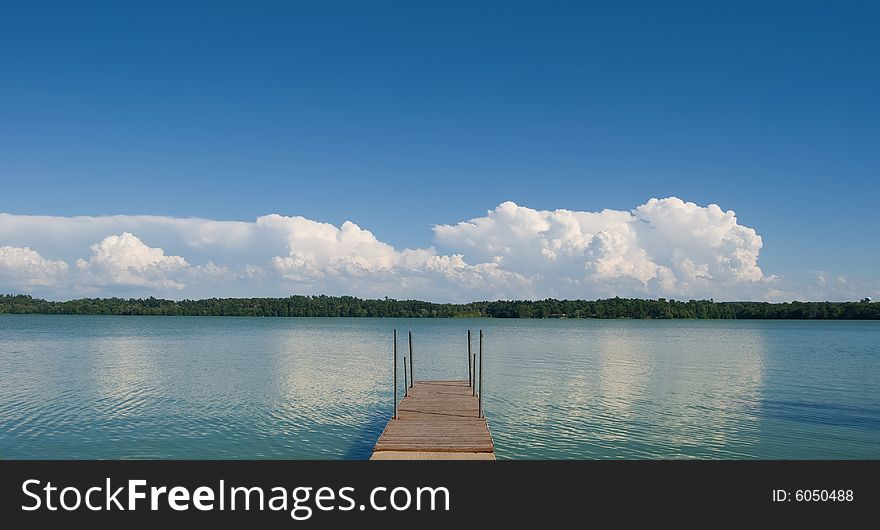 Dock extending out over lake with sky and clouds reflecting off of the waters surface. Dock extending out over lake with sky and clouds reflecting off of the waters surface