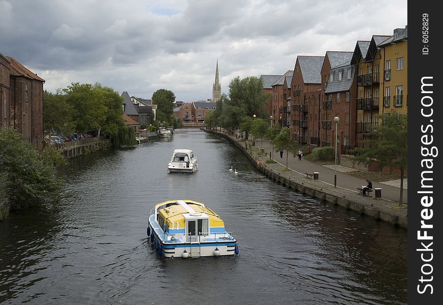 Two boats traveling up the river past the swans heading toward the church spire in the distance. Two boats traveling up the river past the swans heading toward the church spire in the distance