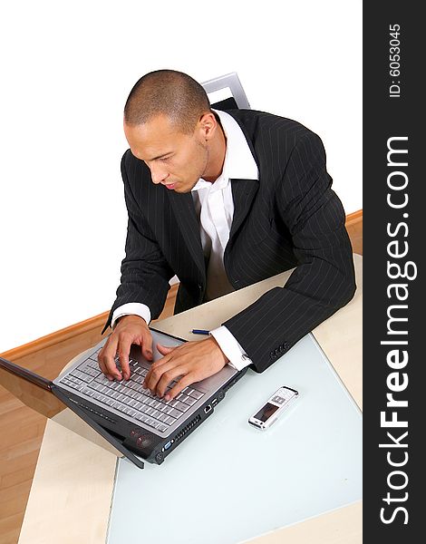 A young businessman sitting by desk at office working on the laptop with cellphone on the table.Isolated over white. A young businessman sitting by desk at office working on the laptop with cellphone on the table.Isolated over white.