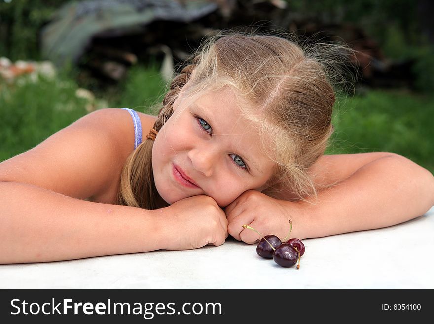 Pretty blond girl sitting near a table with cherries. Pretty blond girl sitting near a table with cherries