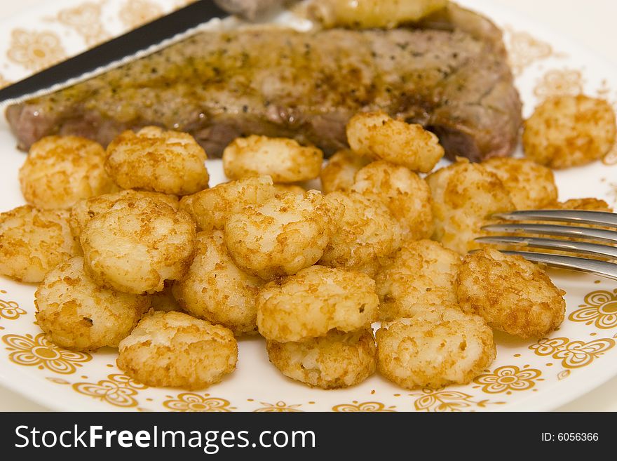 A broiled strip steak on a plate with fried potatoes. A broiled strip steak on a plate with fried potatoes