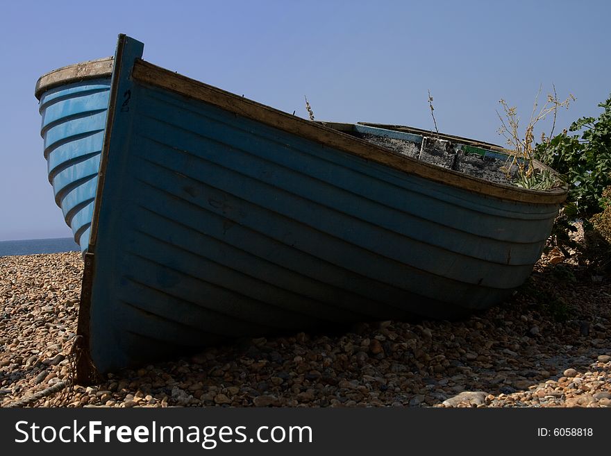 Abandoned old blue fishing boat on pebbled beach