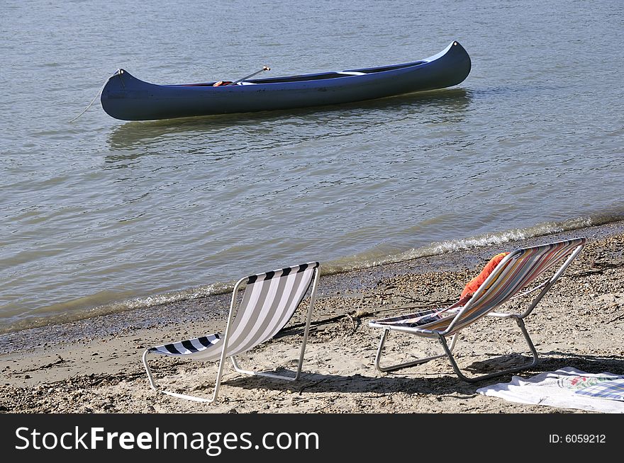 Peaceful deck chairs in bank of a river with a canoe in the background