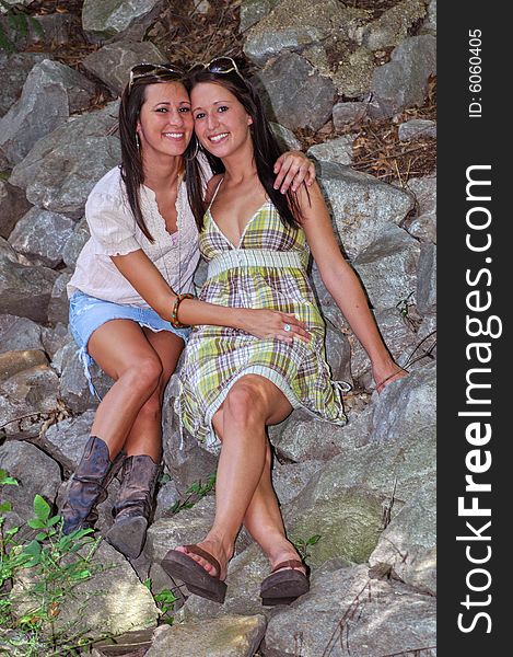 Two young ladies sitting together, hugging on the rocks and smiling happily. Two young ladies sitting together, hugging on the rocks and smiling happily.