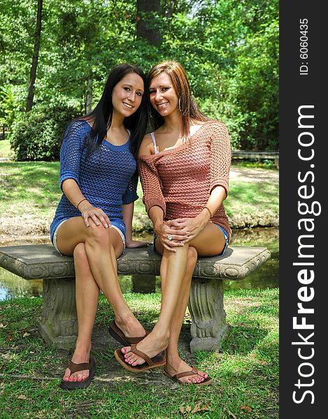 Two young ladies sit on a park bench, smiling. Two young ladies sit on a park bench, smiling.