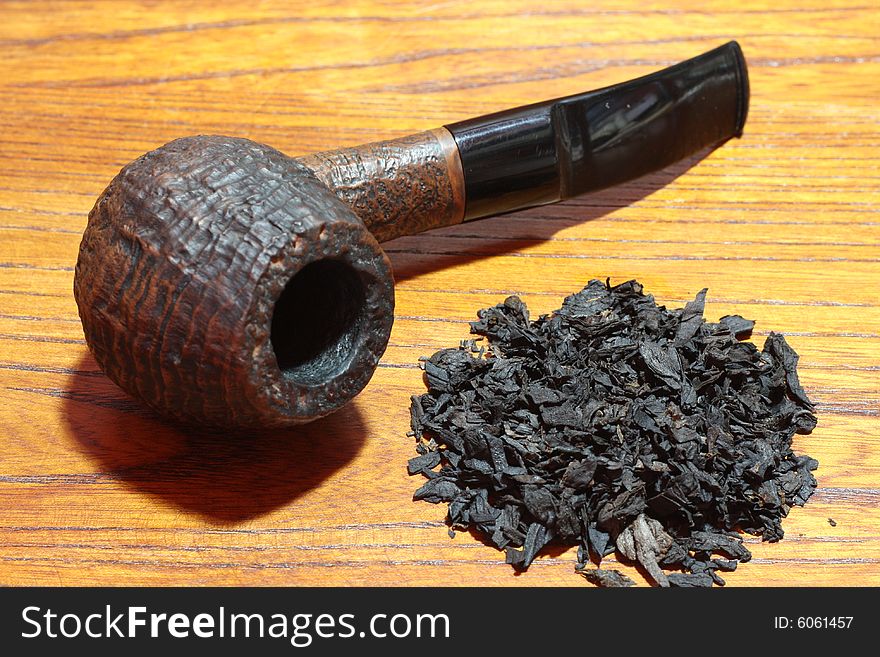 An old tobacco pipe and tobacco on wood background.