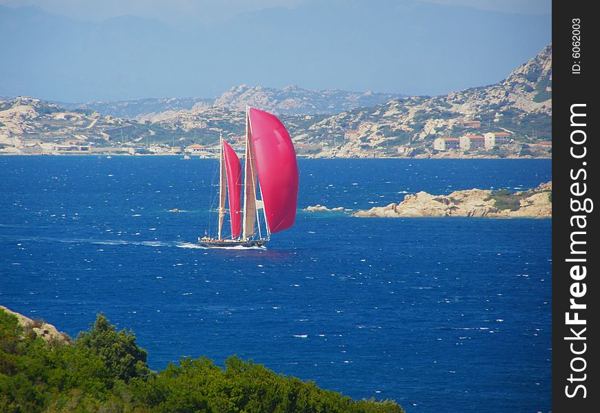 Red sails yacht sailing in the beautiful blue windy sea off the Sardinian coast near Palau, Italy, with wind in its sails